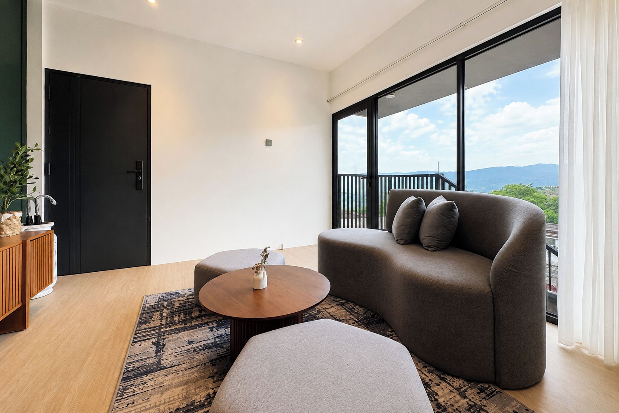 A modern living room with a sofa, ottoman, and coffee table, a wooden cabinet, and a view of the outdoors.
