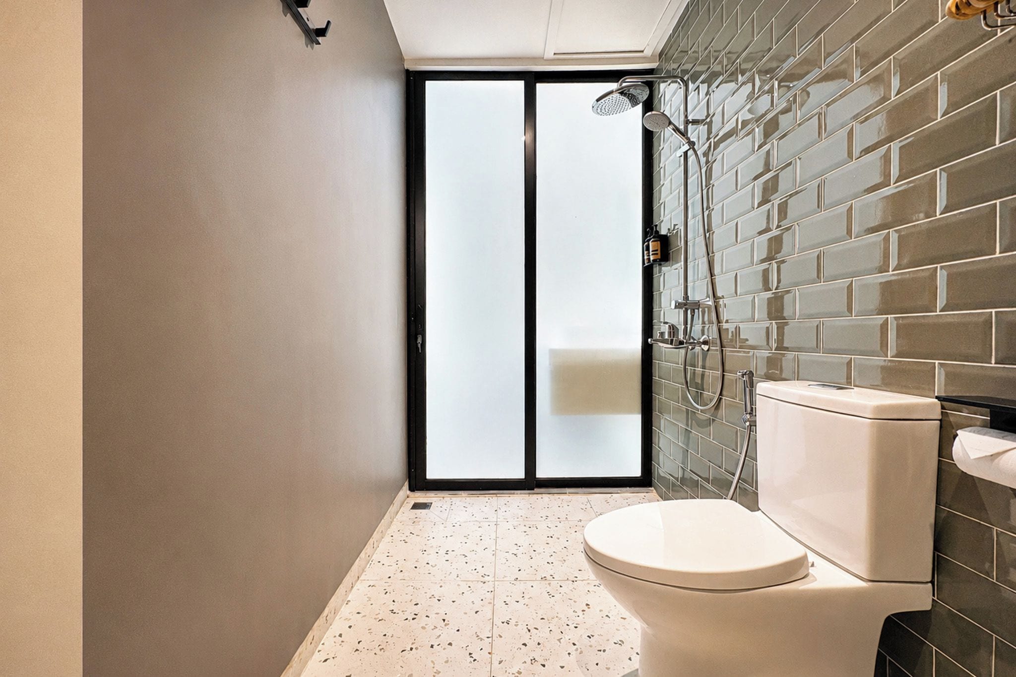 A bathroom with a toilet, a shower, and a tiled wall.