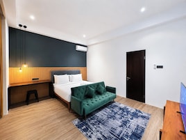 Quarto de hotel moderno com cama, sofá verde, escrivaninha e televisão.