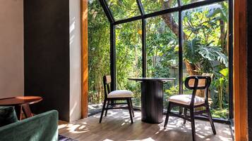 A room with a large window, a round table, two chairs, and a wooden floor.