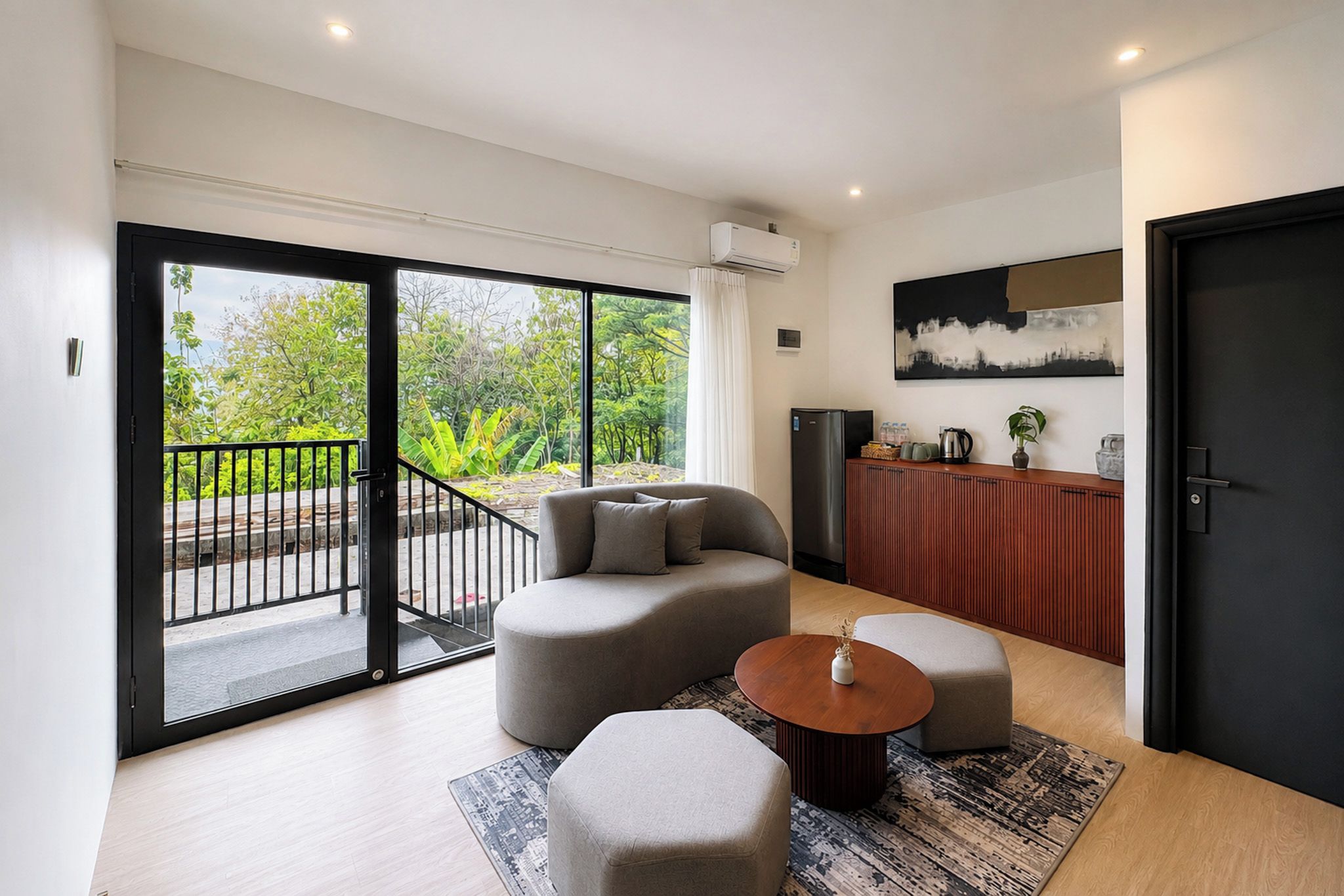 A modern living room with a sofa, ottoman, coffee table, and a view through a sliding glass door to a balcony.