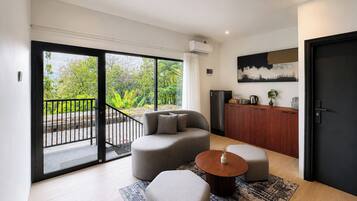 A modern living room with a sofa, ottoman, coffee table, and a view through a sliding glass door to a balcony.