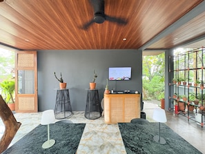 Un interior moderno con techo de madera, mostrador de recepción, dos plantas en macetas, un televisor y una estantería para plantas.