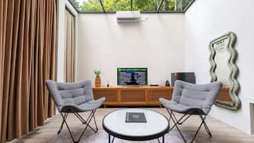 A modern room with a large window, two grey chairs, a small table, and a TV displaying a Spotify chart.