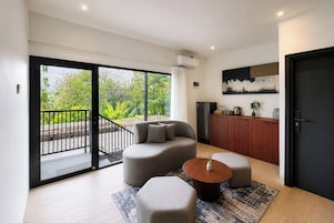 Una sala moderna con sofá, reposapiés, mesa de centro y vistas a un balcón por una puerta corrediza de vidrio.