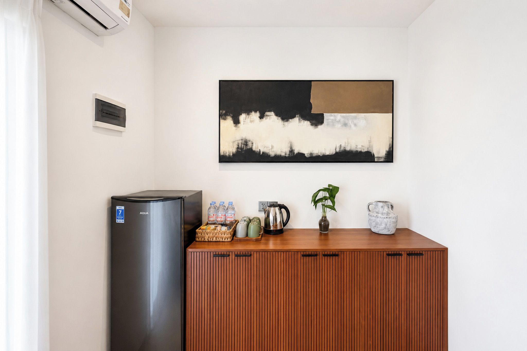 A kitchenette with a refrigerator, a coffee maker, and a plant on a wooden counter.