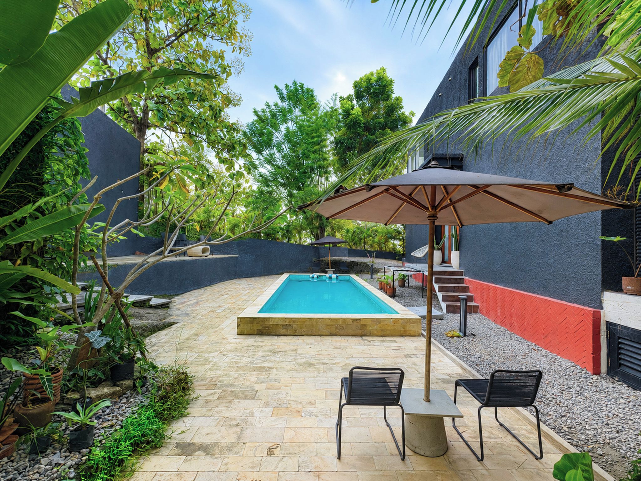 A swimming pool with a tiled deck, surrounded by potted plants and a red wall.
