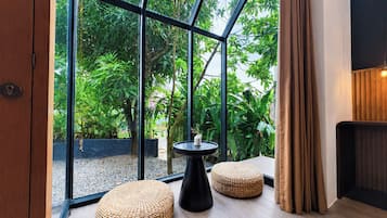 A modern interior with large glass windows, a black table, two woven poufs, and a wooden floor.