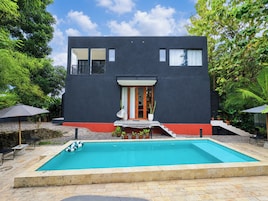 Uma casa moderna de dois andares com piscina, rodeada por vegetação.