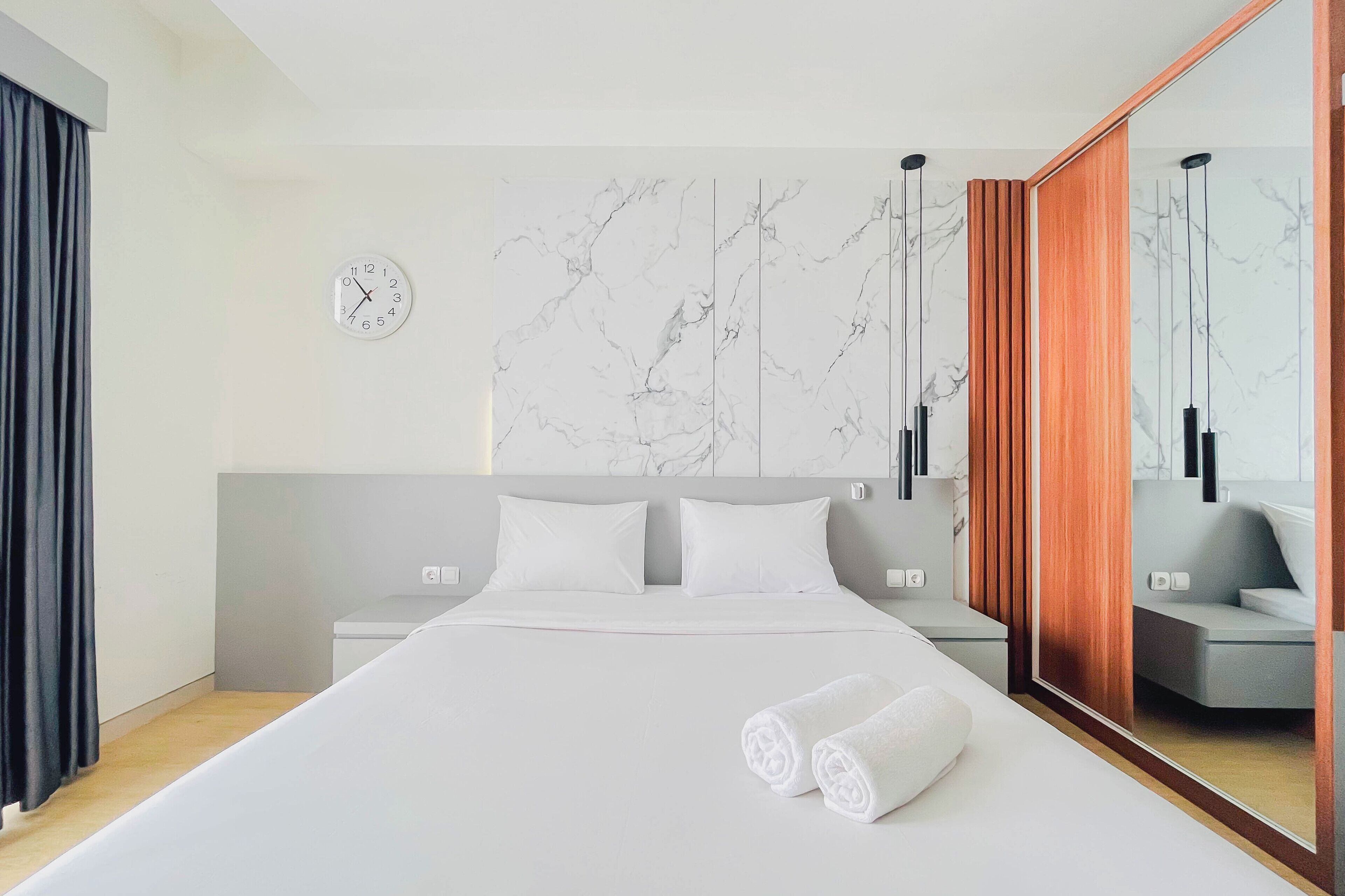 A modern hotel room with a large bed, a marble-patterned wall, a clock, and a mirror.