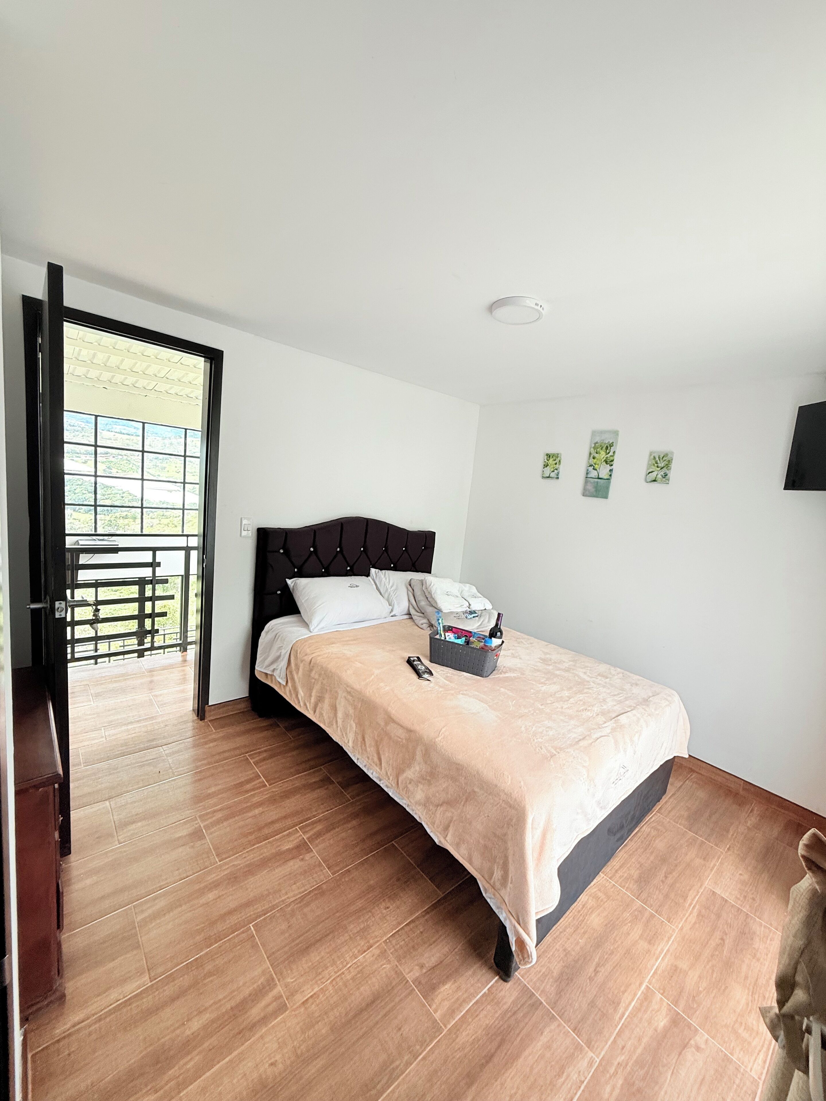 Un dormitorio con cama, mesita de noche, ventana y puerta que da a un balcón.