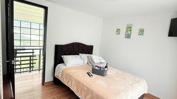 Un dormitorio con cama, mesita de noche, ventana y puerta que da a un balcón.