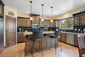 A kitchen with wooden cabinets, a central island with stools, pendant lighting, and a view to the outside.