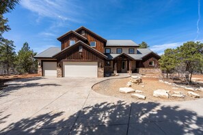 A two-story house with a garage, stone exterior, and a driveway leading to a landscaped area with rocks and trees.