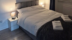 Ein ordentlich bezogenes Bett mit weißen Leinen, einem dunklen Kopfteil und einem Nachttisch mit Lampe.