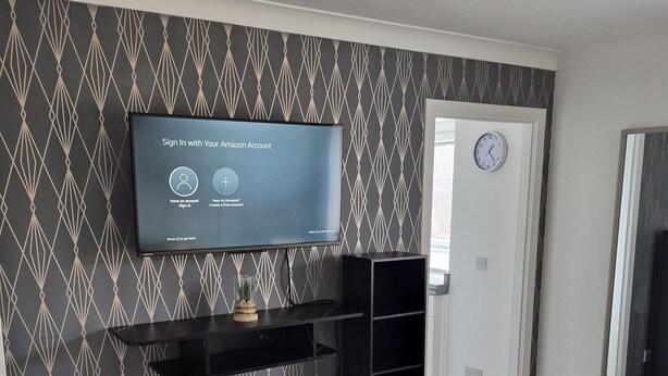 Ein modernes Wohnzimmer mit einem flachbildfernseher an der Wand, einer schwarzen Unterhaltungseinrichtung darunter und einer strukturierten Tapete.