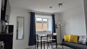 Ein modernes Wohnzimmer mit Essbereich, einem Sofa mit gelben Kissen und einem Fernseher auf einem Lowboard.