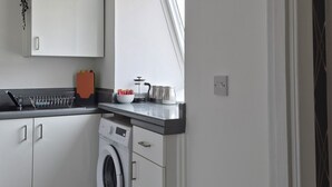Eine moderne Küche mit weißen Schränken, einer Waschmaschine, einem Spülbecken und einer Uhr an der Wand.
