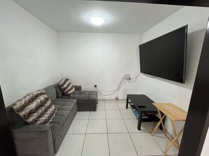 A living room with a grey sofa, a small table, and a TV mounted on the wall. - Tremendous 4-bedroom house with AC in charming Tijuana (Tijuana)