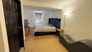 Een slaapkamer met een bed, nachtkastje, lamp en een stoel.