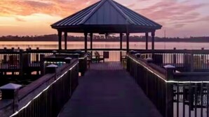 A wooden pier leading to a gazebo with a view of a sunset over a body of water. -  Sunrise lake view from the balcony. 3-bedroom condo near Disney/universal. (Orlando)