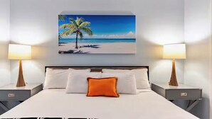 A hotel room with a bed, two bedside tables, a nightstand, a wall-mounted painting of a beach scene, and two lamps. -  Sunrise lake view from the balcony. 3-bedroom condo near Disney/universal. (Orlando)