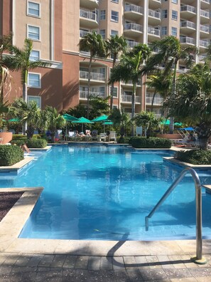 A swimming pool with a metal ladder, surrounded by palm trees and a multi-story building with balconies. - Beach front two bedroom condo (Noord)
