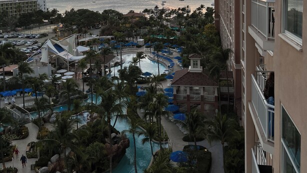 Um resort com várias piscinas, palmeiras e vista para o oceano ao pôr do sol.