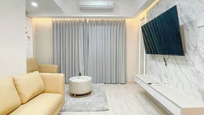 Una sala de estar moderna con un sofá, una mesa redonda de centro, un televisor montado en la pared y un amplio ventanal con cortinas.