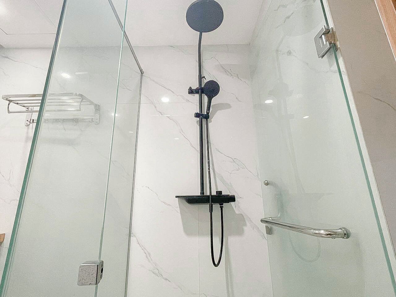 Una ducha con cerramiento de vidrio, un cabezal de ducha manual y un panel de control en la pared.