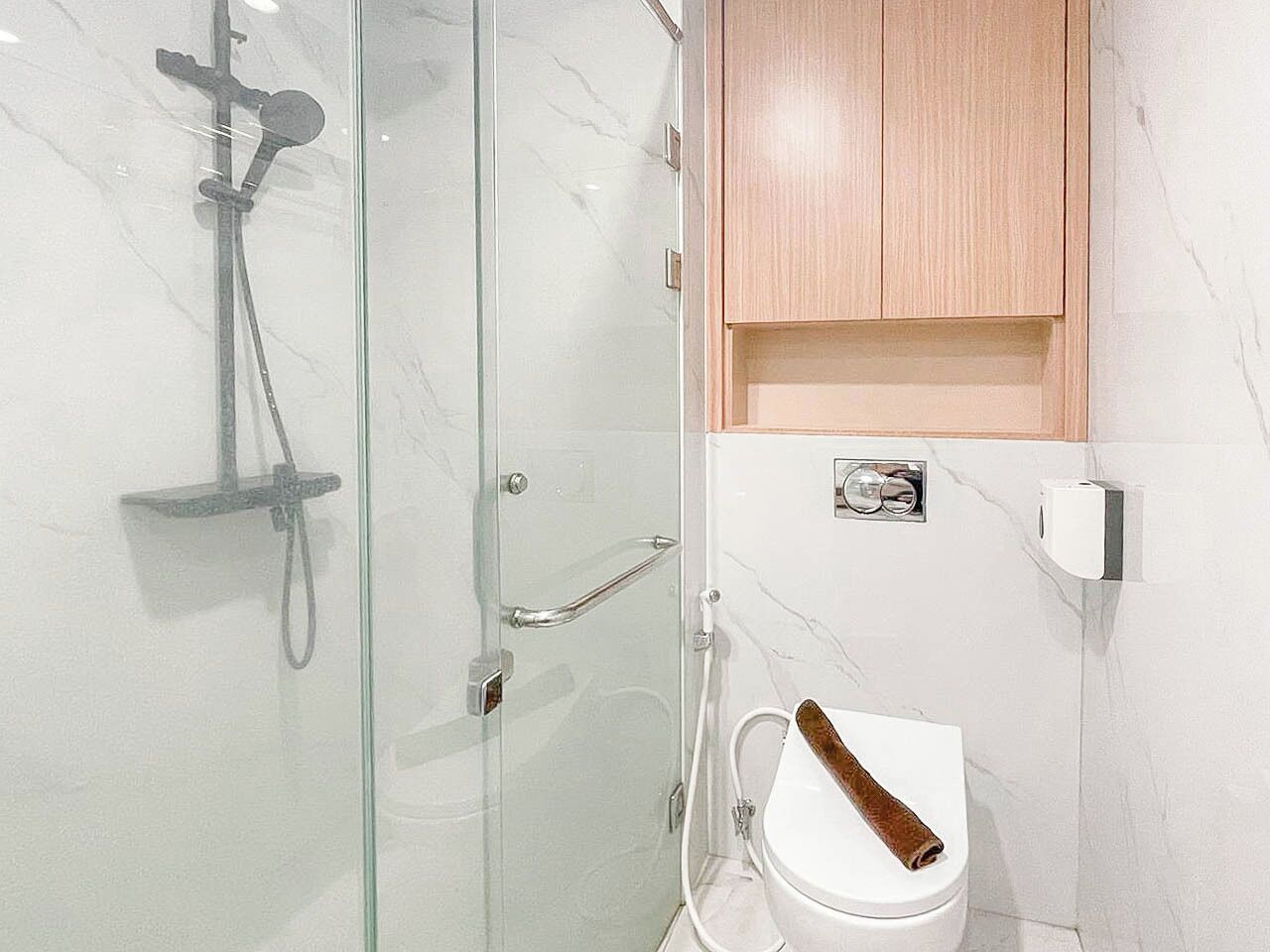 Une salle de bain avec une douche à parois de verre, des toilettes blanches et un meuble en bois placé au-dessus des toilettes.