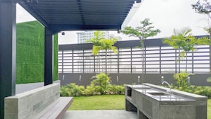 Un área exterior moderna con asientos, una banca, un lavabo y un pequeño jardín con palmeras.