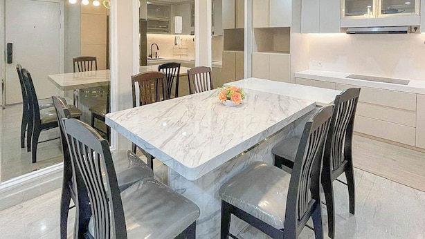 Una cocina moderna con una isla de mármol, electrodomésticos integrados y un comedor con sillas y una mesa.