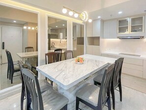 A modern kitchen with a marble island, built-in appliances, and a dining area with chairs and a table. - Functional 3BR at Apartment Podomoro City Deli Medan (Medan)