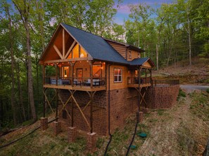 A wooden cabin with a stone foundation, a balcony, and a covered porch area. - New Build! 2B-2B Secluded Cabin/Hot Tub/Games/EV/Parking (Sevierville)