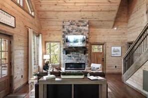 A wooden cabin interior with a stone fireplace, a television mounted above it, and a cozy seating area with a sofa and a coffee table. - New Build! 2B-2B Secluded Cabin/Hot Tub/Games/EV/Parking (Sevierville)