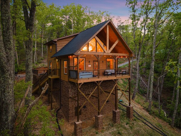 A cabin with a stone foundation, wooden upper structure, and a balcony with outdoor seating. - New Build! 2B-2B Secluded Cabin/Hot Tub/Games/EV/Parking (Sevierville)