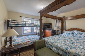 Quarto com beliche, uma cama de solteiro, cabeceira de madeira, escrivaninha com abajur e televisão.