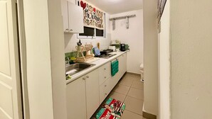 Cocina compacta con armarios blancos, un lavamanos, una encimera con varios objetos y una ventana sobre el lavamanos.