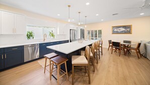A modern kitchen with a large island, dark blue cabinets, white countertops, and wooden chairs. - 3229 Managed by Brampton Park (Pompano Beach)