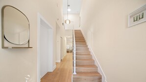 A hallway with a wooden staircase, a round mirror on the wall, and a hanging light fixture. - 3229 Managed by Brampton Park (Pompano Beach)