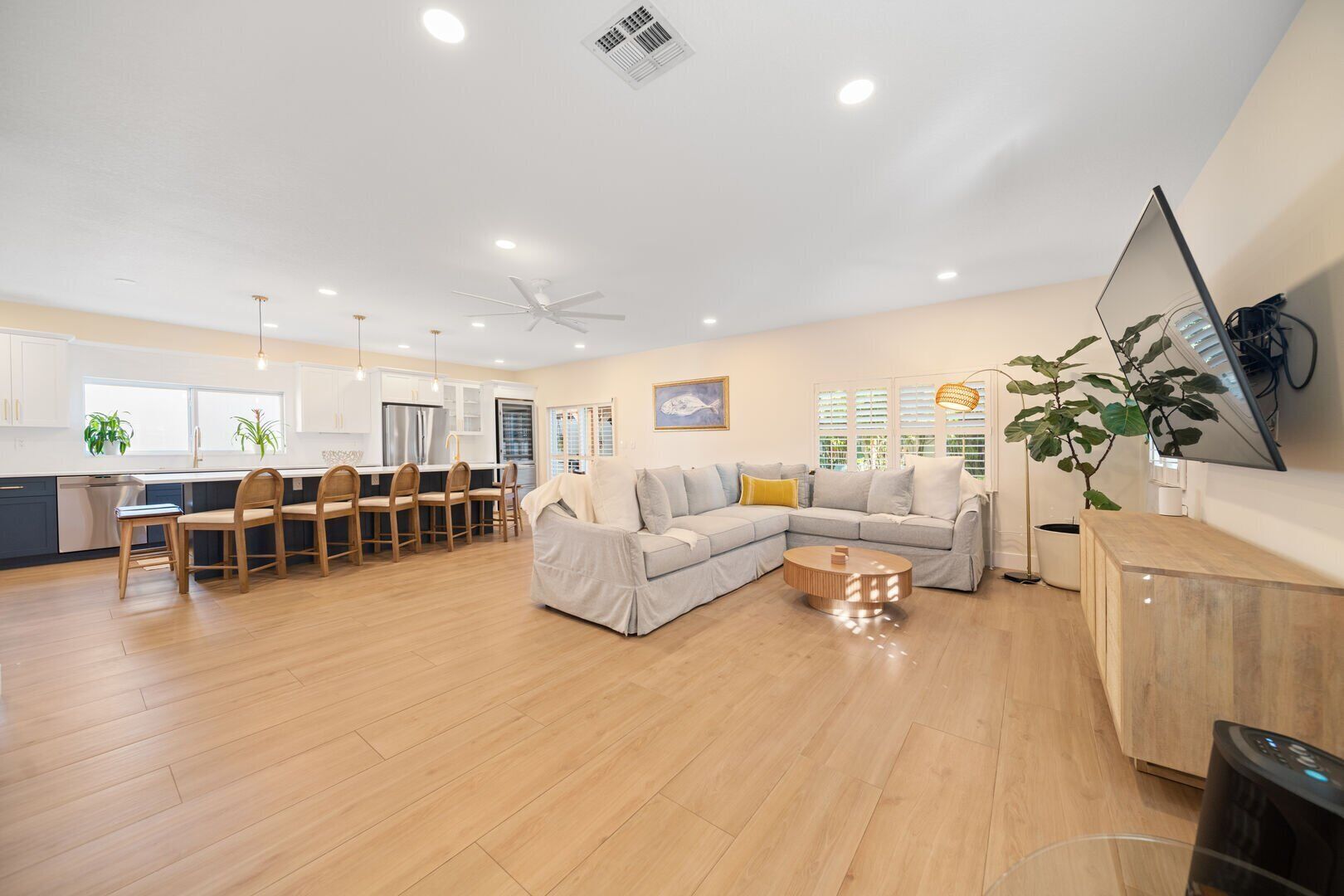 A spacious living area with a large L-shaped sofa, a dining table with chairs, and a kitchen in the background.
