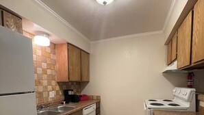 A compact kitchen with wooden cabinets, a white refrigerator, a dishwasher, a stove, and a tiled backsplash.