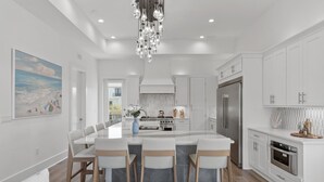 Une cuisine moderne dotée d’un îlot central, de meubles blancs, d’appareils électroménagers en acier inoxydable et d’un lustre.