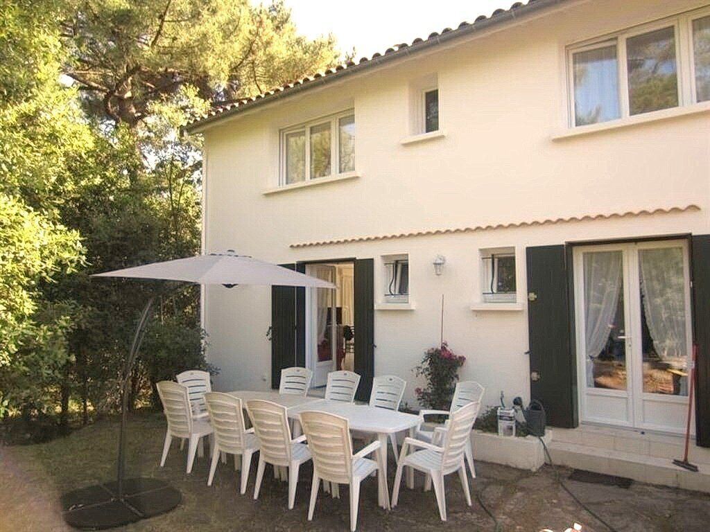 A two-story house with a patio area featuring a table and chairs, a white umbrella, and a small garden.