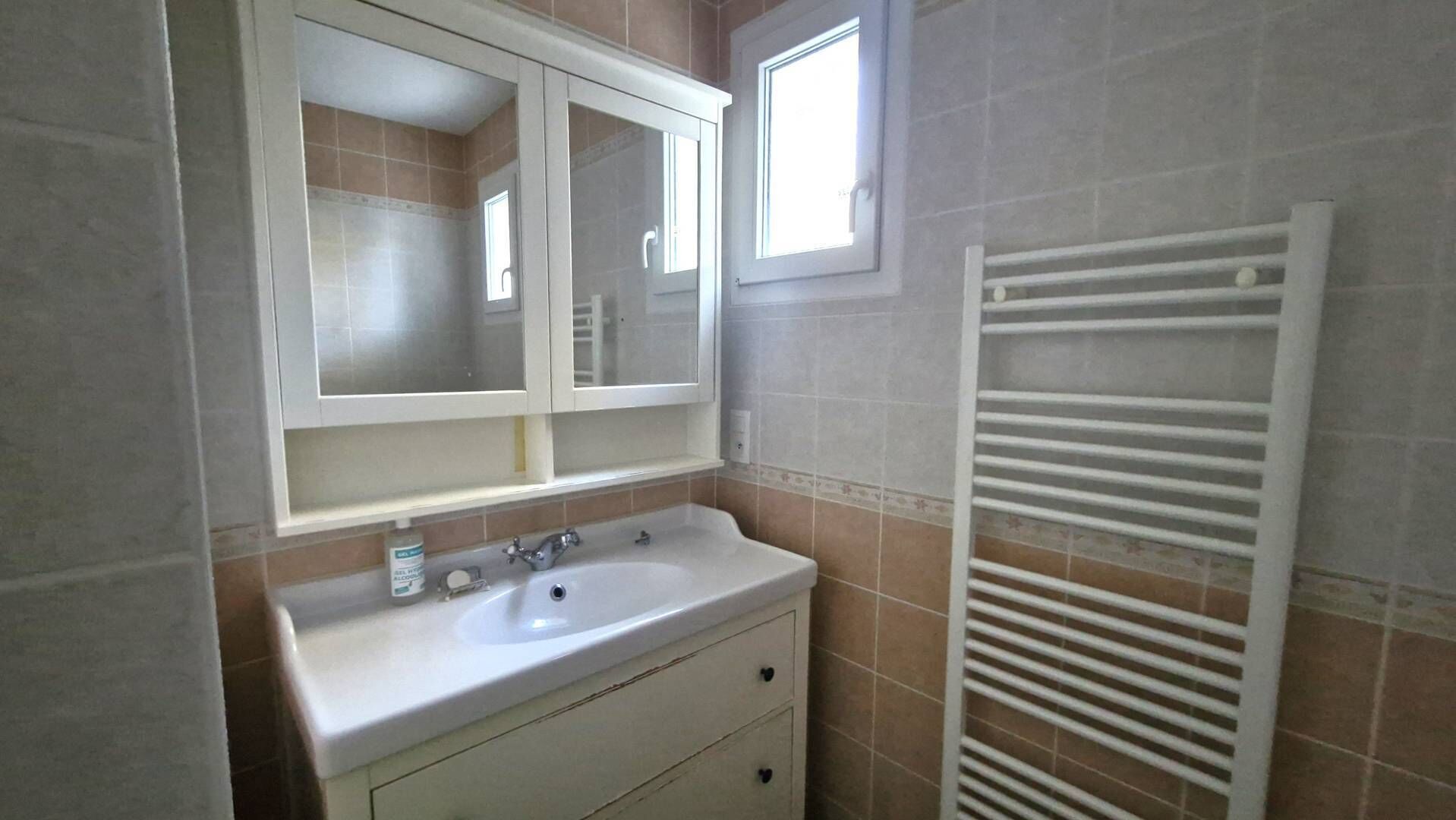 Un baño con lavamanos blanco, espejo y toallero.