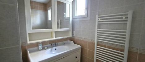Un baño con lavamanos blanco, espejo y toallero.