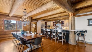 A spacious kitchen with wooden beams, a dining area with a large table and chairs, and a view of the outdoors. - Log Masterpiece with 5 Master Suites, Pool Table, Hot Tub (Silverthorne)