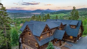 A large log cabin with multiple rooms, surrounded by a mountainous landscape and a lake. - Log Masterpiece with 5 Master Suites, Pool Table, Hot Tub (Silverthorne)