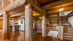 A spacious log cabin interior with a central wooden staircase, a kitchen area, and a dining space. - Log Masterpiece with 5 Master Suites, Pool Table, Hot Tub (Silverthorne)